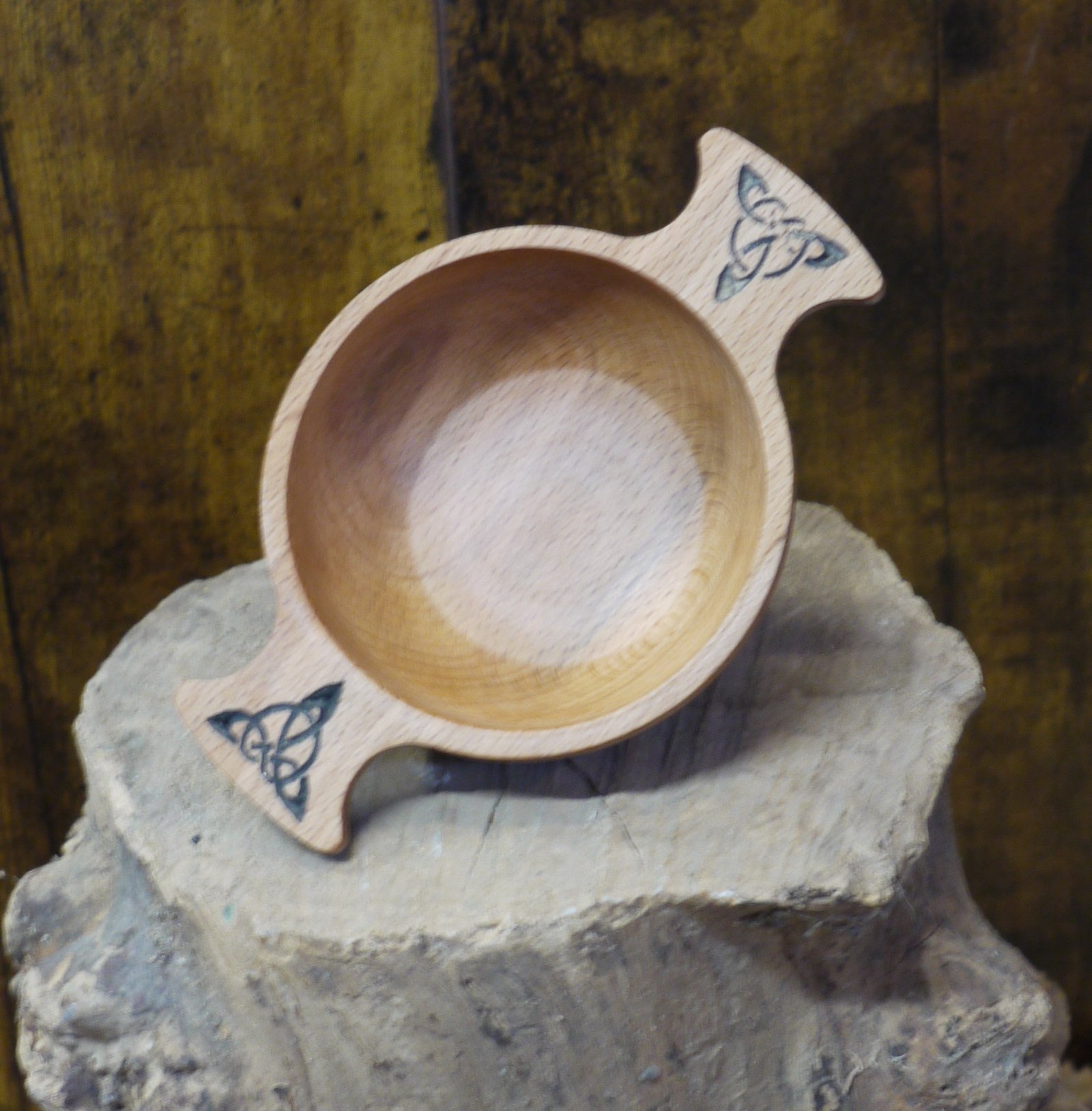 Traditional Scottish quaich with celtic pattern displayed on a log